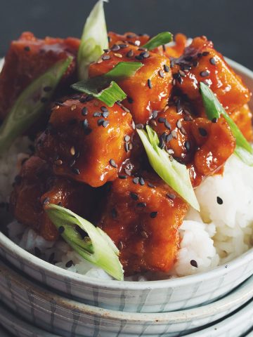 a portion of sweet and sour tofu on rice in a bowl garnished with green onion