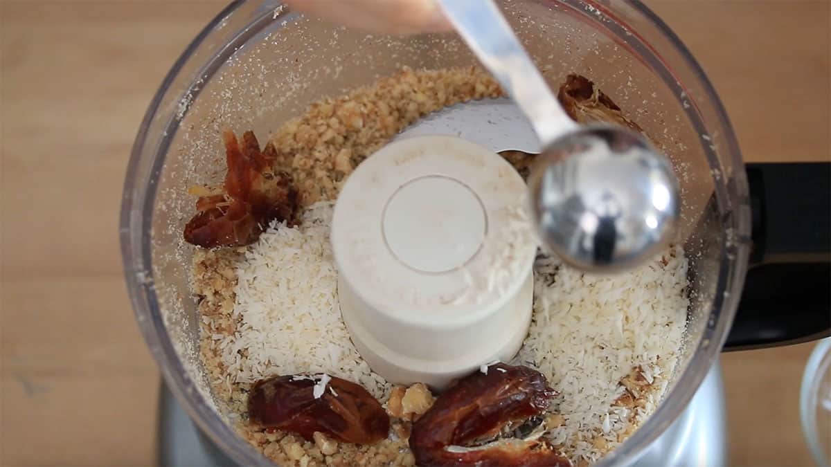 overhead of food processor with crushed walnuts and dates and coconut being added