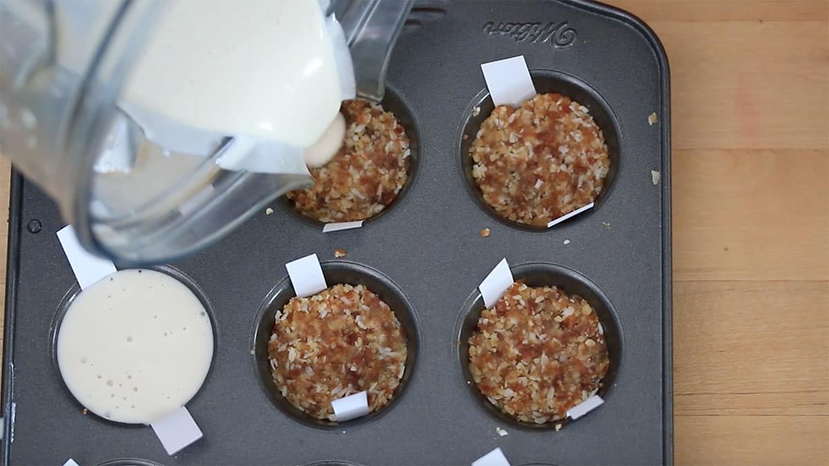 vegan cheesecake mix being added to mini muffin pan cups on top of the crust
