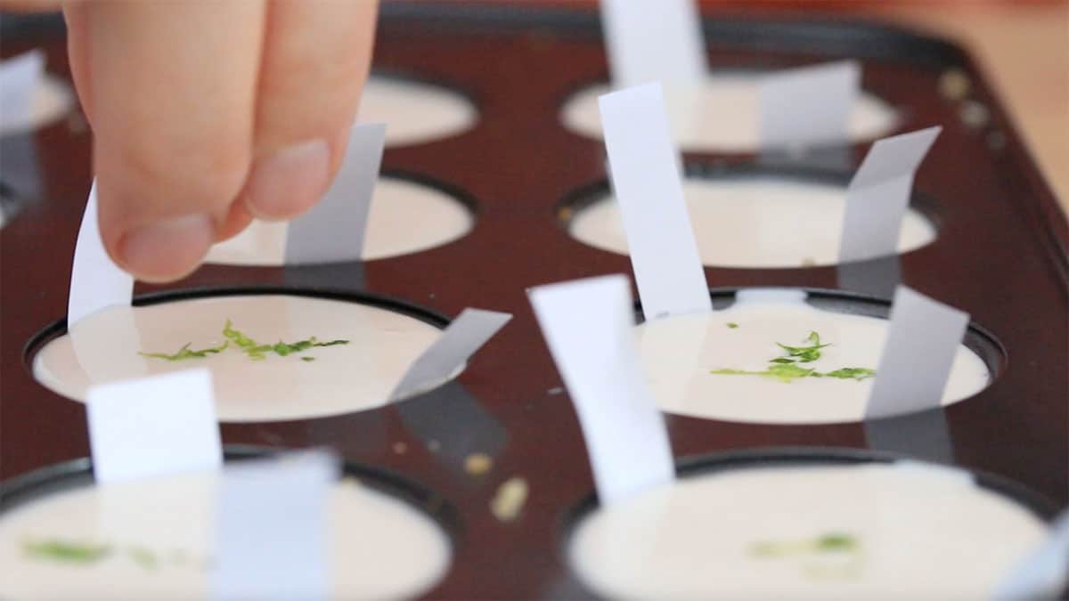 side angle of mini muffin pan cups filled with vegan cheesecake being garnished with lime zest