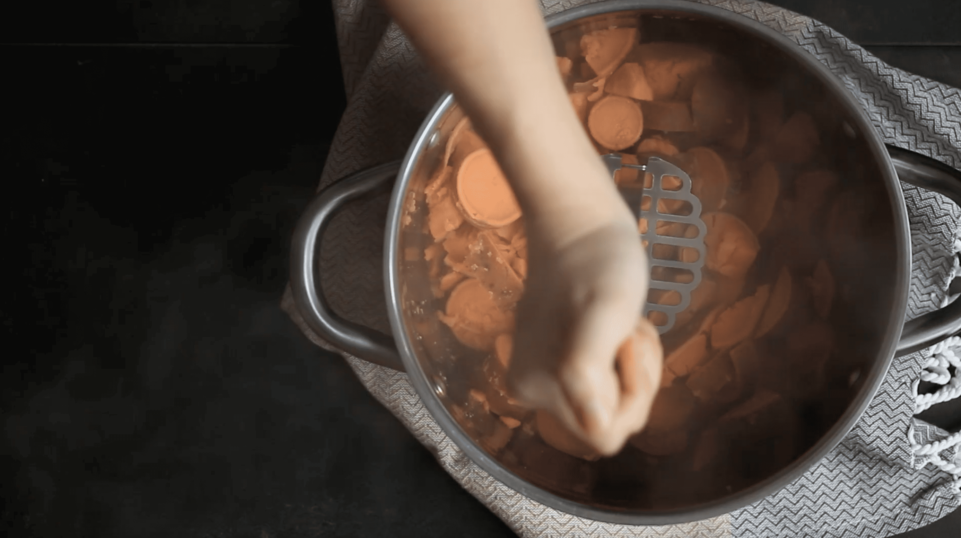 hand mashing sweet potatoes in a pot