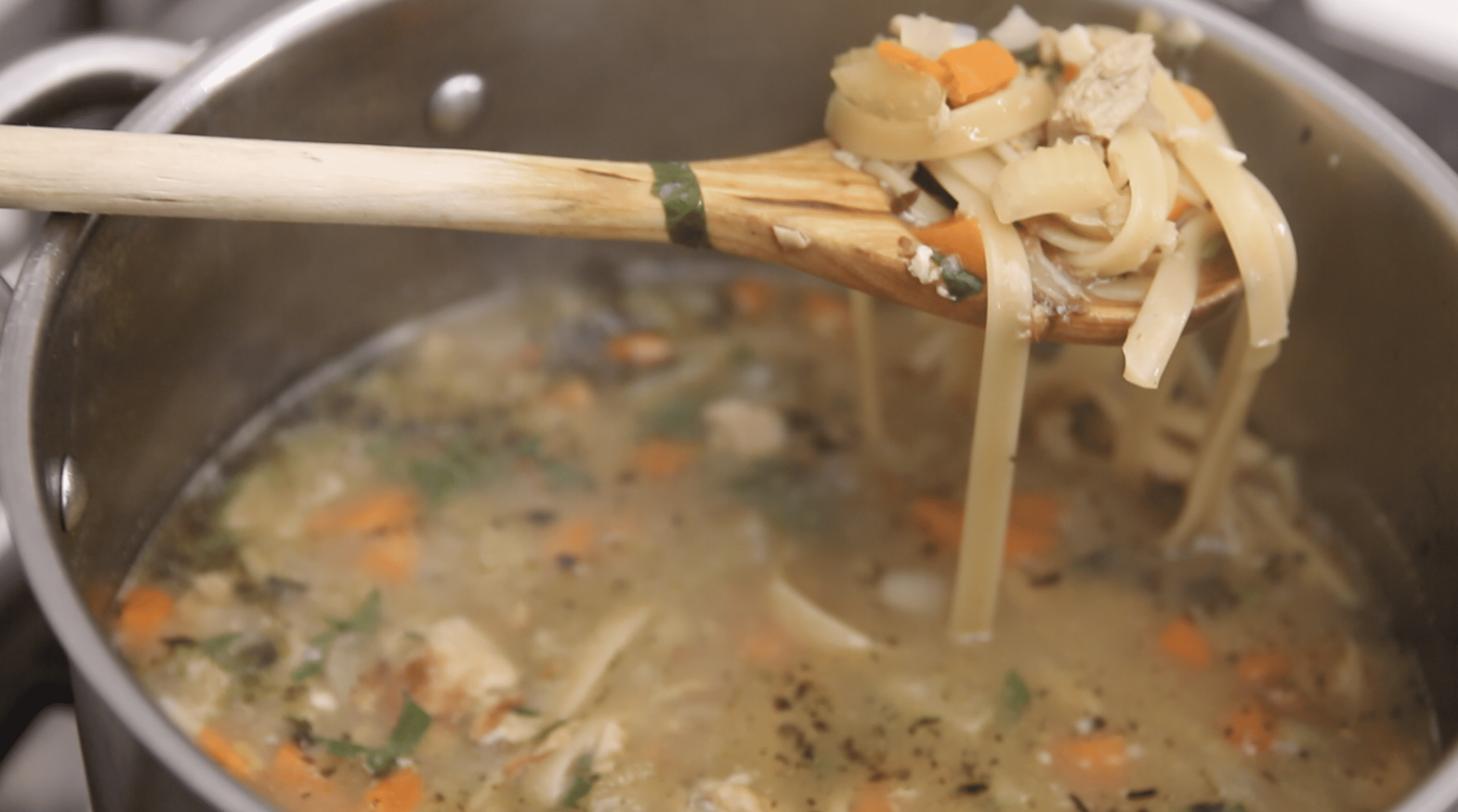 spoon serving vegan chicken noodle soup from a pot