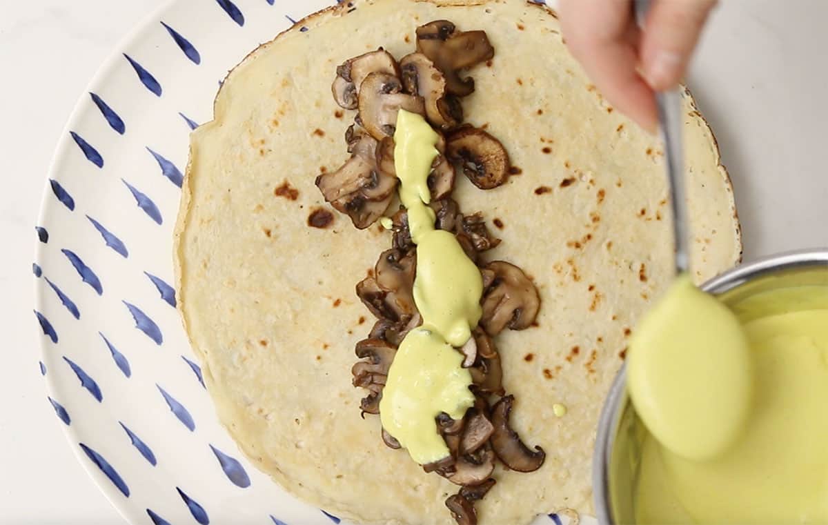 a crepe on a plate with mushrooms and hollandaise on top