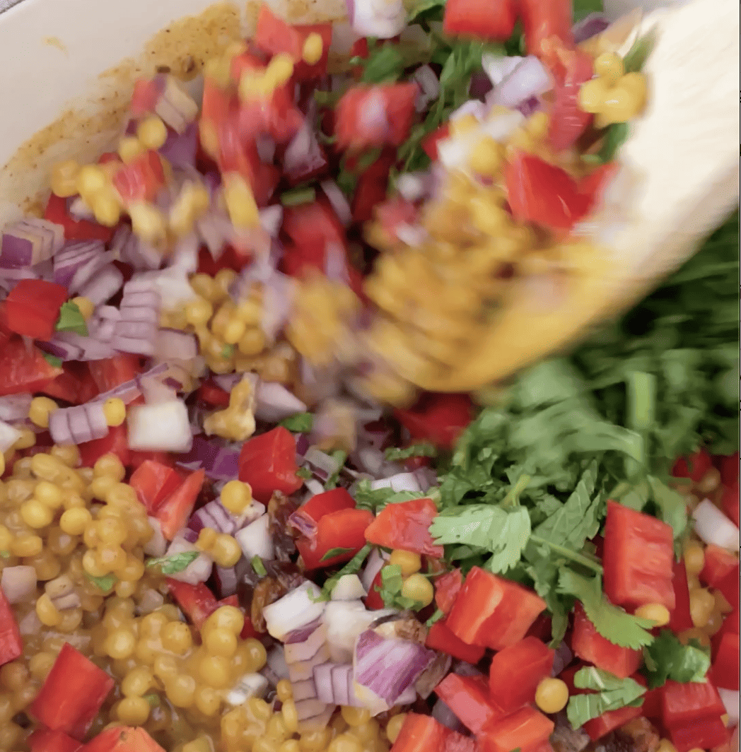 fresh ingredients being stirred into cooked couscous