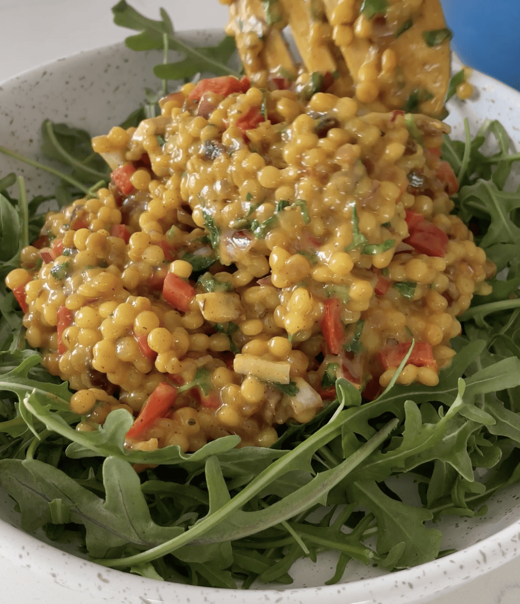 warm couscous being spooned onto ned of arugula