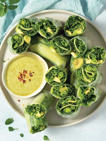 overhead of a plate of halved green fresh rolls with dipping sauce