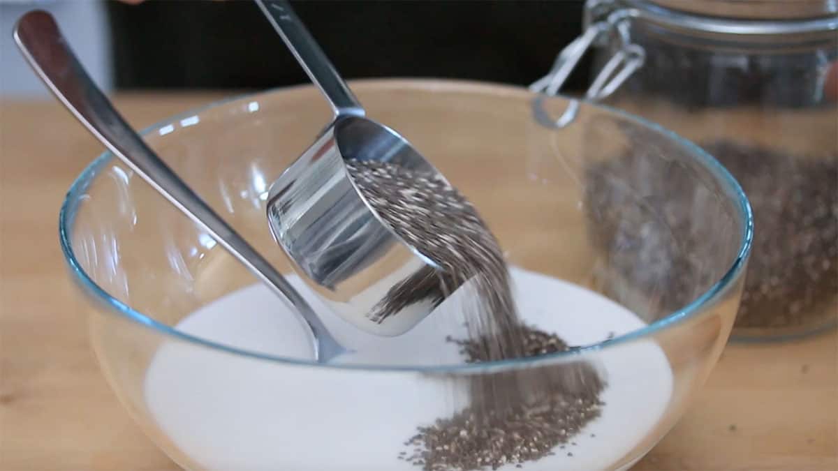 mixing bowl with coconut milk in it and a cup of chia seeds being added